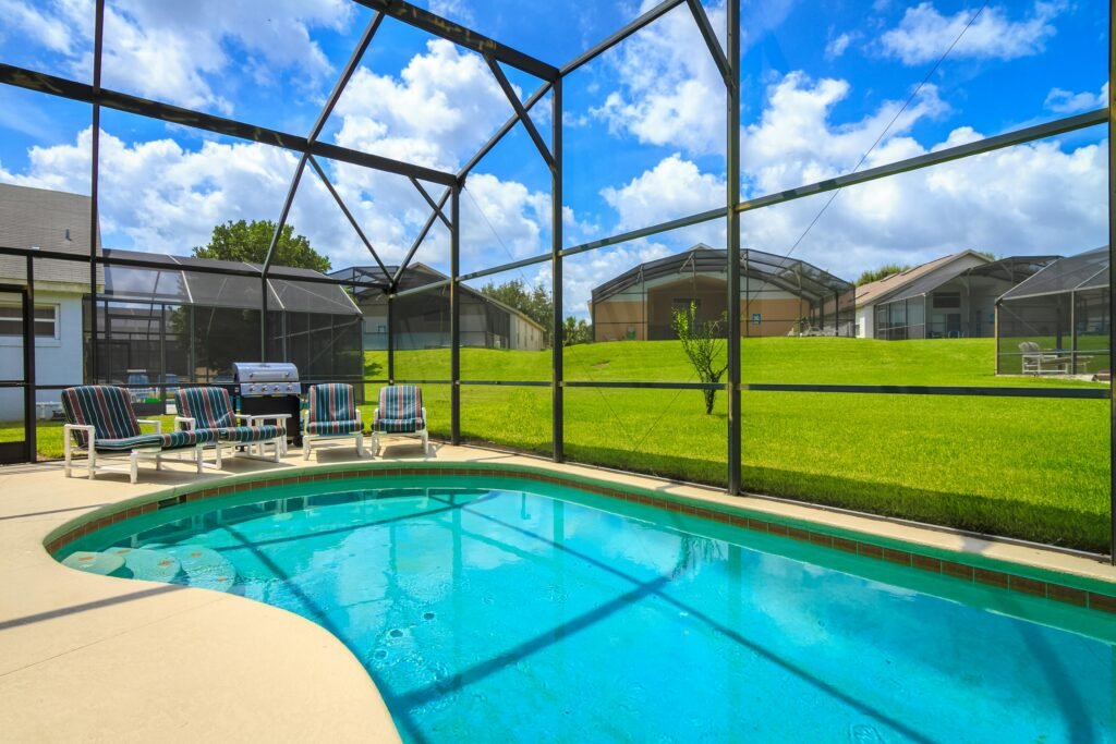 A sunny outdoor enclosed pool at a Florida villa with lounge chairs and a grill, perfect for relaxation.